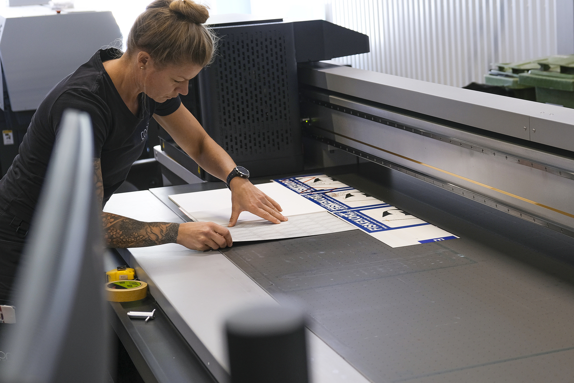 Bild på Skyltmakaren Sara Arvén som förbereder en produktion i en av Concils planprintrar. Bordet har ett antal olika vakuumzoner som stabiliserar skyltämnet.
